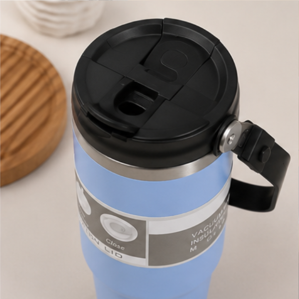 Light blue insulated travel mug with black flip-top lid and carry handle, silver vacuum-insulated band detail
