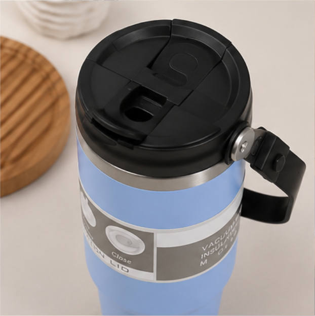 Light blue insulated travel mug with black flip-top lid and carry handle, silver vacuum-insulated band detail