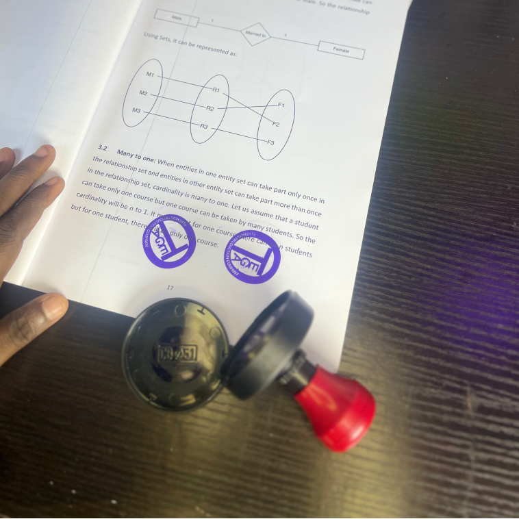 Two custom rubber stamps with blue ink impressions on an open textbook, one stamp has a red handle